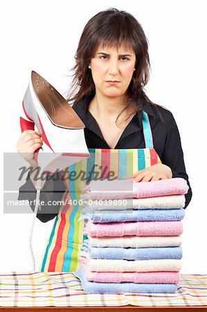 Furious housewife in apron holding a eletric iron close to towels stacked