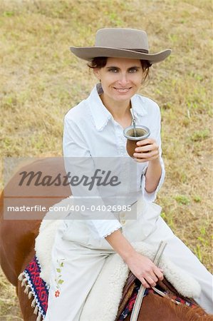 A young Argentinean gaucha relaxing with yerba mate while riding her horse.