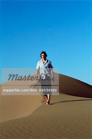 Young man walking along sand dune
