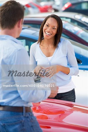 Young woman talking to car salesman in lot