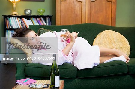 A young woman lying on her couch drinking wine