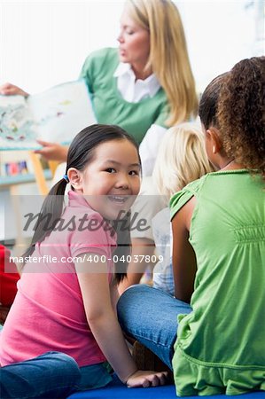 Kindergarten teacher reading to children in library, girl lookin