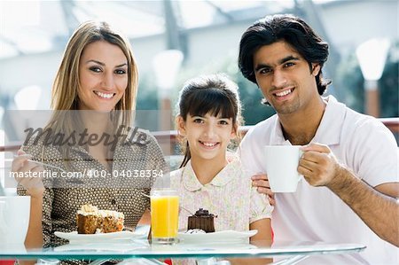 Family eating cake in cafe looking to camera
