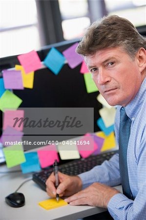 Businessman in office at monitor with notes on it writing