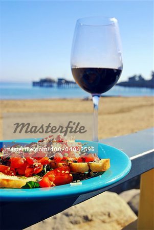 Glass of red wine and plate of fresh bruschetta on a restaurant's deck railing by the ocean beach