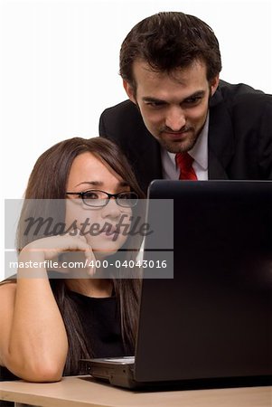 Attractive brunette woman sitting on a desk in front of laptop computer with a man coworker standing behind her both looking at screen