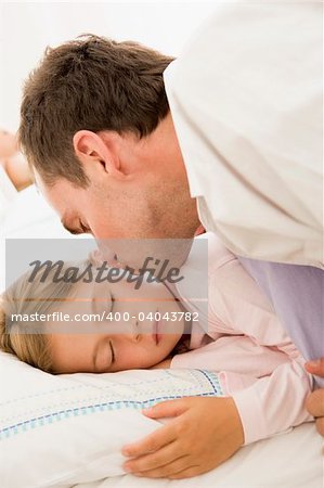 Man waking young girl in bed with kiss