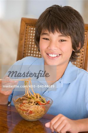 Young boy in dining room eating chinese food smiling