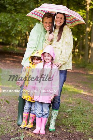 Family outdoors in rain with umbrella smiling