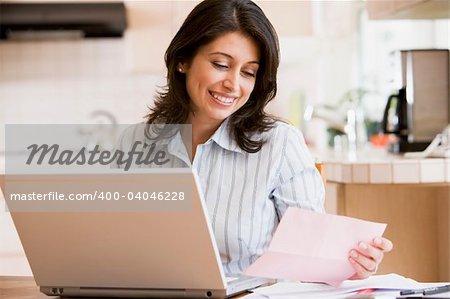 Woman in kitchen with laptop smiling