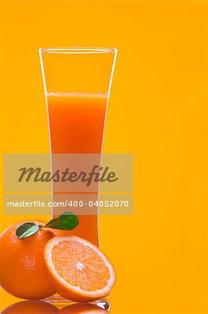 View of long glass filled with fresh juice and some oranges nearby