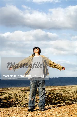 freedom - teenager male with arms wide open, shirt and hair blowing in the wind, standing atop a 1,000 foot cliff