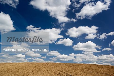 Blue sky with clouds over ploughed field.