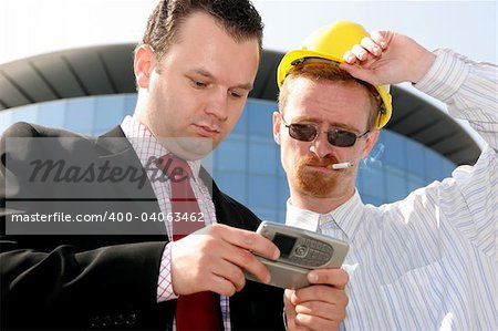 Young businessman showing something on a cell phone(PDA), to a construction worker in front of a corporate building