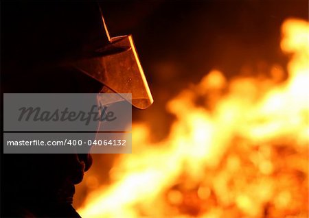 Silhouette of a firefighter facing a blazing fire