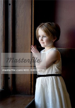Pretty little girl looking out a large window and wearing a pretty dress.