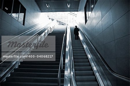 Single female moving against the light in escalator - Berlin Central Station. - Duotone.