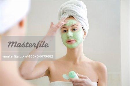 Young woman applying green algae facial mask.