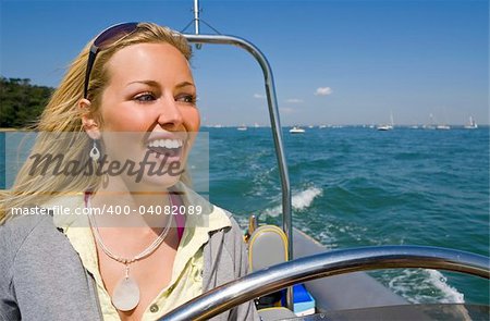 A stunningly beautiful young woman driving a powerboat and having fun in a beautiful sun drenched coastal location.