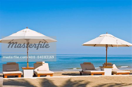 Idyllic scene of deck chairs under an umbrella on a clean beach in the hot afternoon sun.