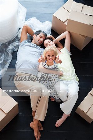 Parents and daughter on the floor of their new house with thumbs up