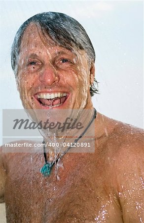 a colour portrait of a happy laughing forties man having a wash under a shower outdoors