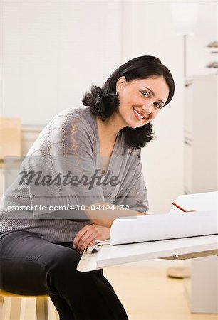 Attractive brunette woman drawing on white paper on board, smiling at camera. Vertical