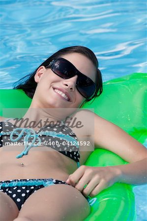 Attractive slim and tanned young lady lying on inflatable sunbed on sunny swimming pool on vacation or holiday