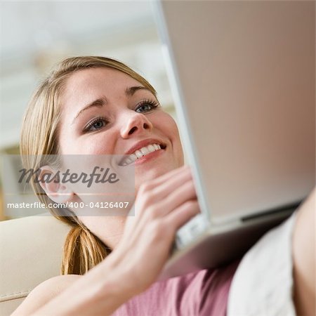 Attractive blonde woman relaxing with laptop computer.Smiling, looking at the laptop.Square.