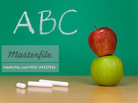 ABC written on a chalkboard. Some chalks and a red apple over a green one on the foreground.