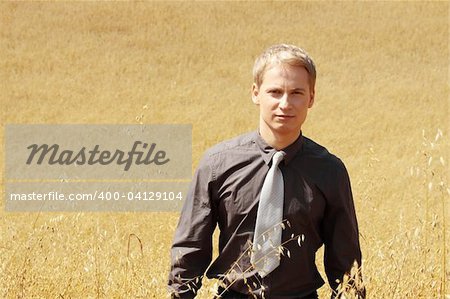 Young modern farmer in suit standing in field of oats