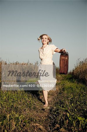 Young happy woman with a suitcase running on a rural road.