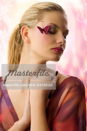 Beautiful woman in fashionable dress with creative makeup with butterfly on her face and closed eyes