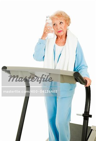Senior woman on a treadmill cools down with bottled water.  Isolated on white.