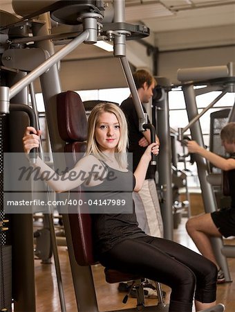 Girl using an exercise machine at a health club with two men in the background