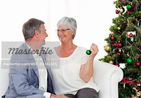 Mature couple sitting on sofa with a Christmas tree in the background