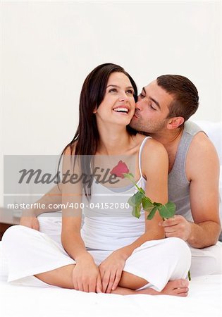 Happy lovers sitting on bed with a rose