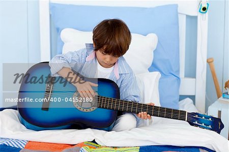 Happy little boy playing guitar in bed