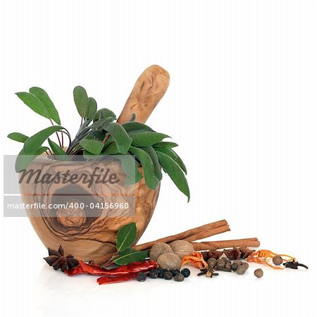 Sage herb leaves in an olive wood mortar with pestle and a selection of spices over white background.