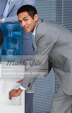 Attractive businessman filling cup from water cooler in the office