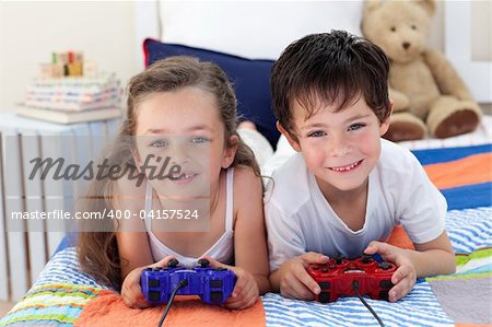Siblings playing video games together and lying on bed