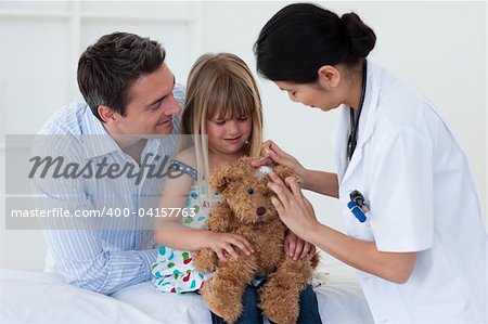 Portrait of a doctor and little girl examing a teddy bear in the hospital