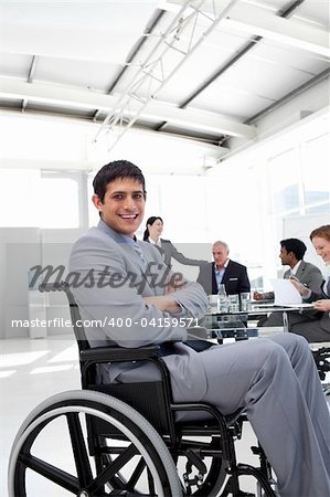 Attractive businessman sitting in a wheelchair  with folded armsat a meeting