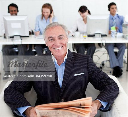 Senior manager reading a newspaper with his team in the background