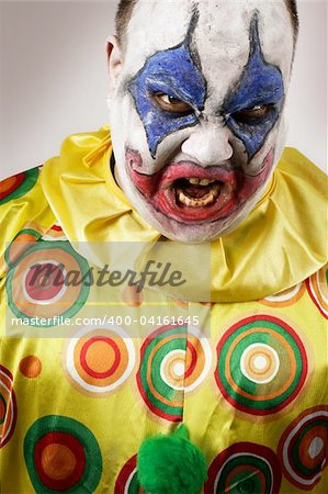 A nasty evil clown, angry and looking mean. Harsh lighting, focus on the teeth.