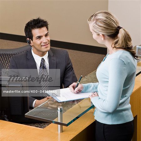 Businesswoman talking to receptionist.  Square framed shot.