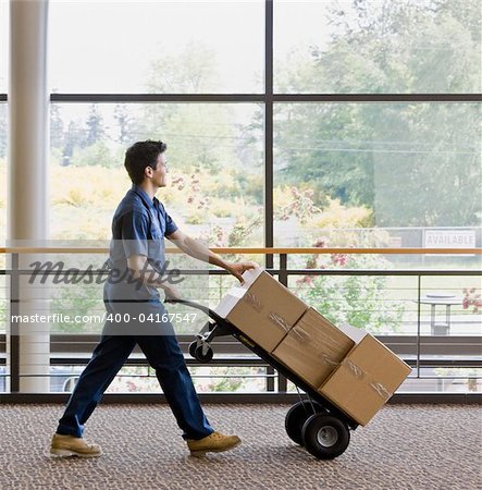 Young man using hand truck to move boxes.  Vertically framed shot.