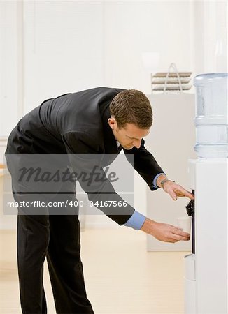 Business man getting water from water cooler. Vertically framed shot.