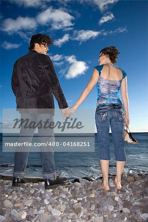 Rear view of a young couple standing on the beach holding hands. Vertical shot.