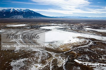Aerial view of a snowy, rural landscape with mountains in the distance. Horizontal shot.